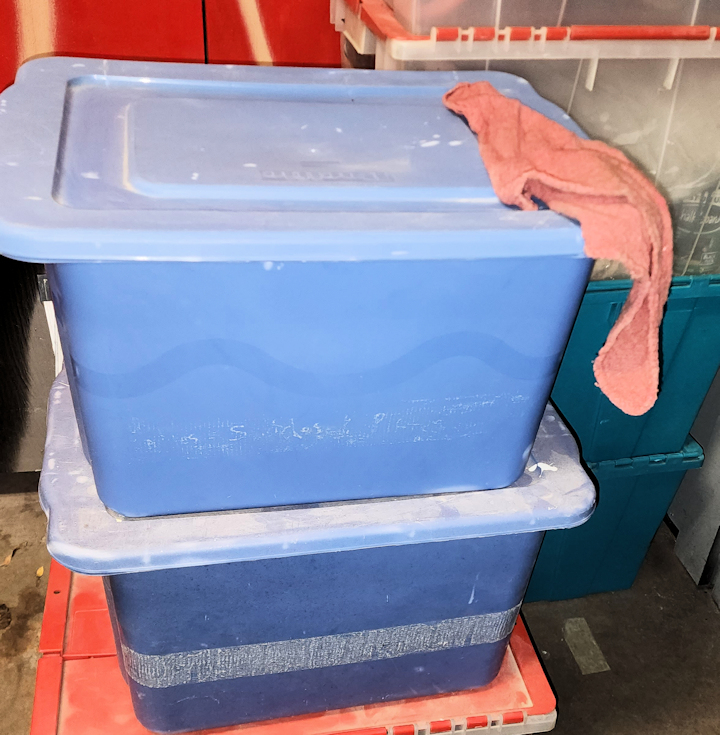 Blue stackable bins labeled with an invoice number, used to organize engine parts during repair